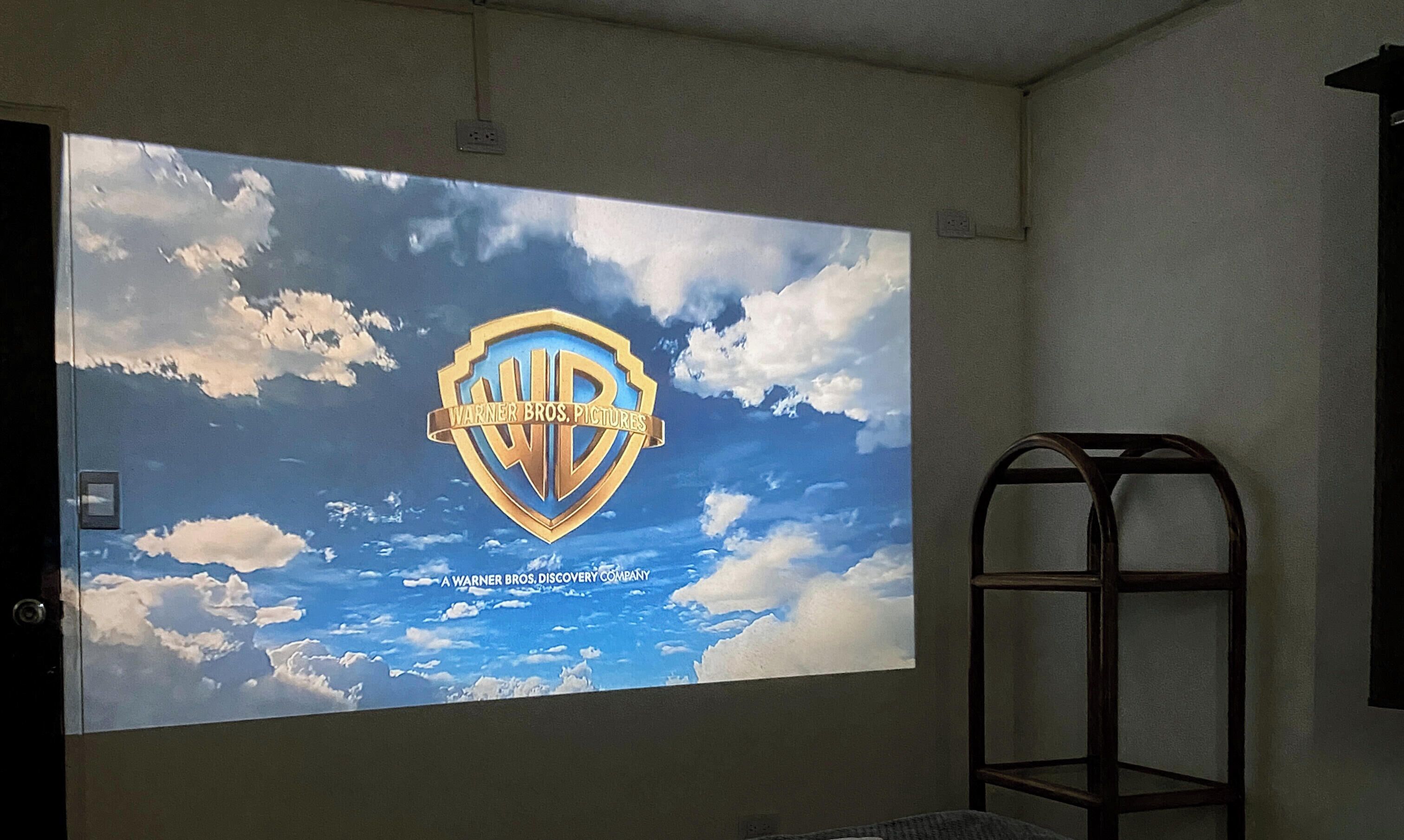 A projector screen displaying the Warner Bros. Pictures logo against a sky backdrop.