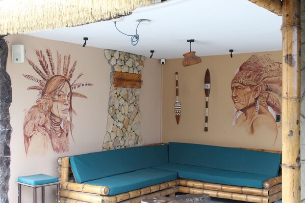 A room with a stone wall, a blue cushioned sofa, and a mural with indigenous artwork. - Grand ilama Hotel (Cali)