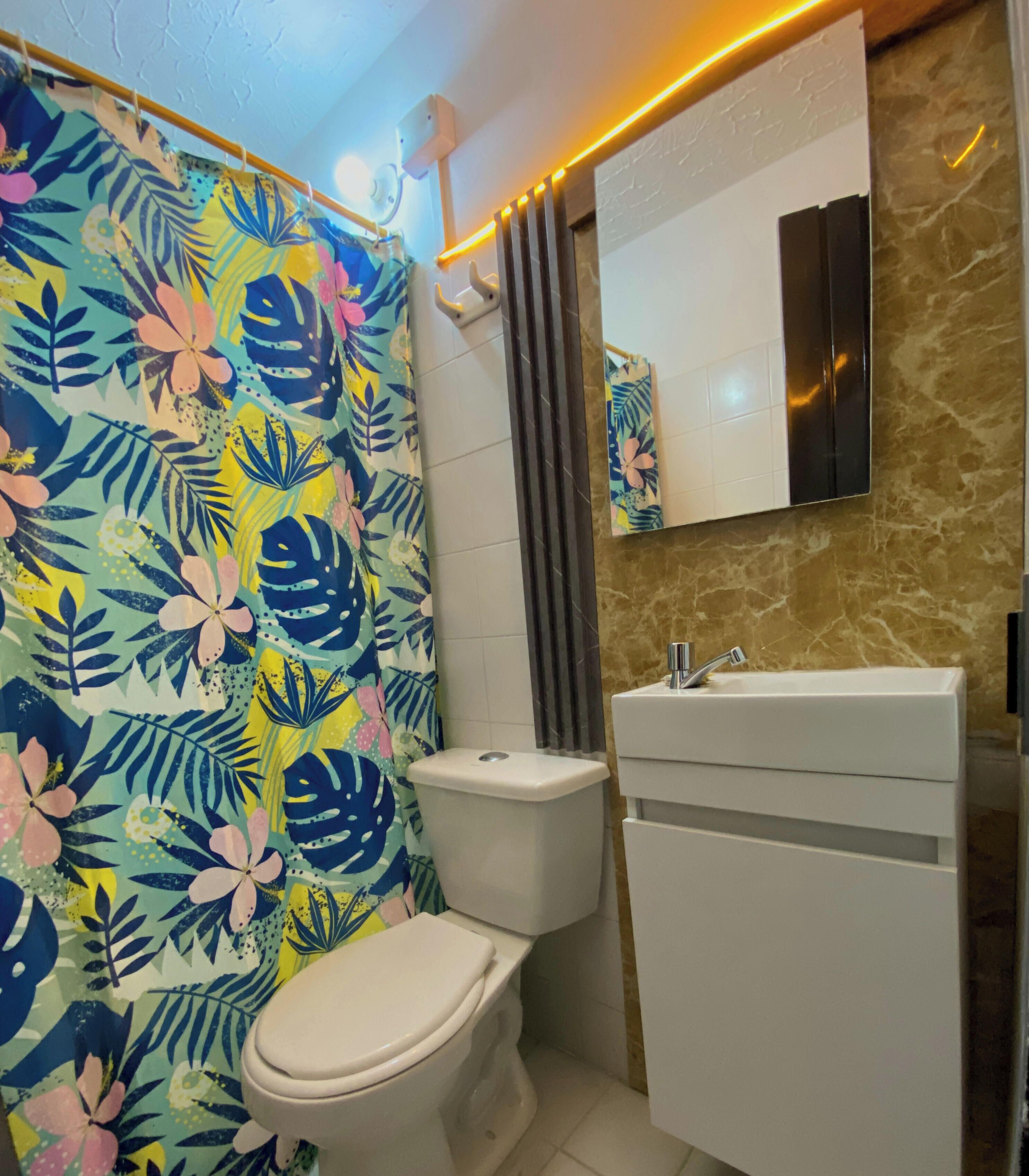 A bathroom with a toilet, a sink, and a shower curtain with a tropical leaf pattern.