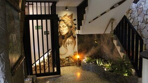 A hallway with a stone wall, a mural, a staircase, and a fire extinguisher. - Grand ilama Hotel (Cali)