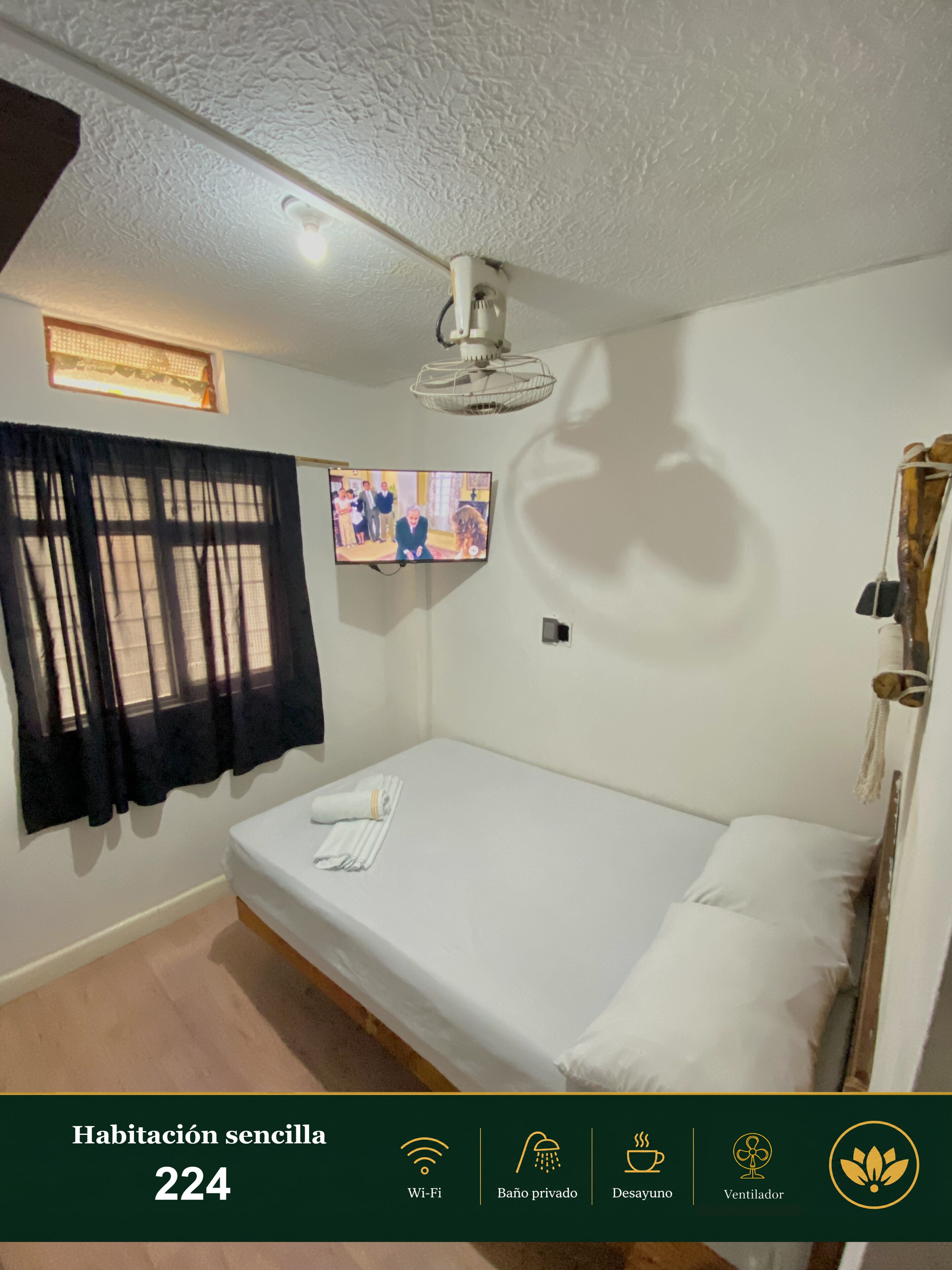 A simple room with a bed, a TV, and a ceiling fan.