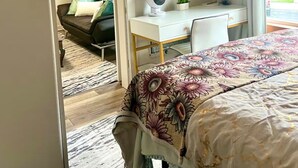 Une chambre à coucher avec un lit, un bureau, une chaise, un miroir et une fenêtre avec des rideaux.