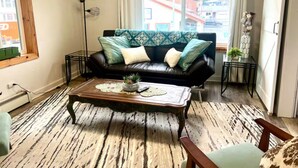Un salon avec un canapé en cuir noir, une table basse en bois et un tapis à motifs.