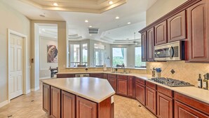 A spacious kitchen with a large island, dark wooden cabinets, and a modern stainless steel microwave.