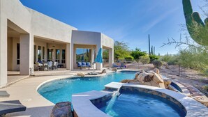 A modern outdoor pool area with a hot tub, lounge chairs, and a covered seating area.