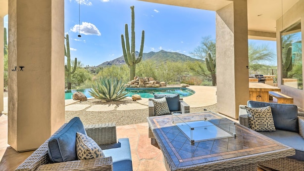 A patio area with outdoor furniture, a pool, and a view of a desert landscape with cacti and mountains.