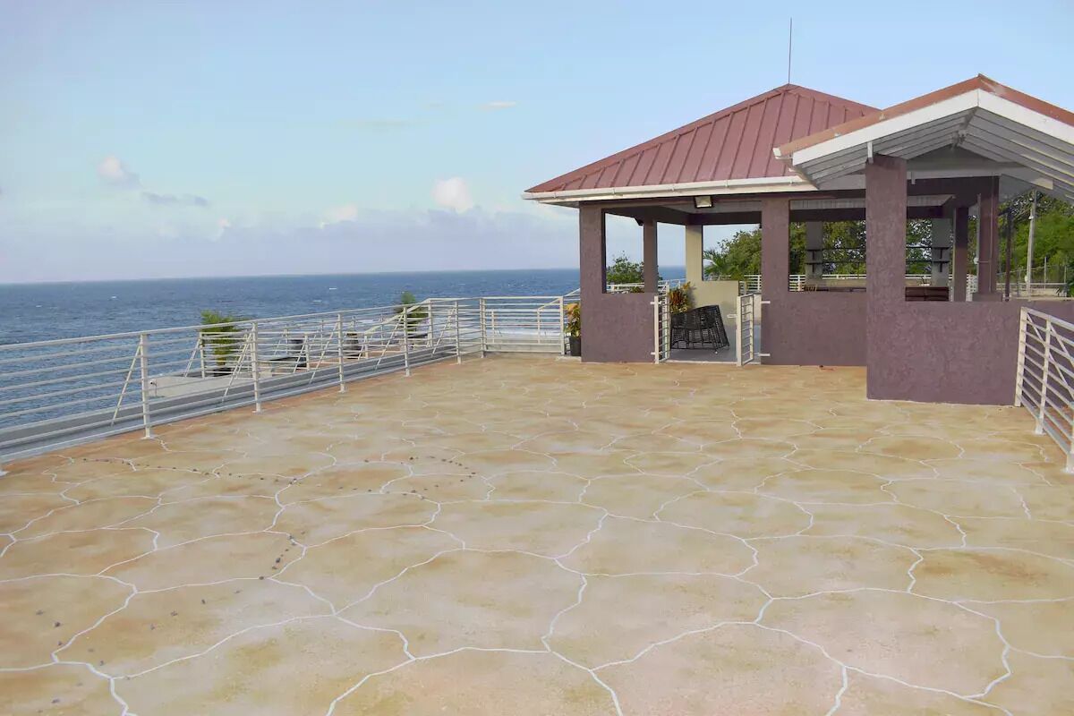 A covered outdoor area with a stone floor and a metal railing, overlooking the sea.