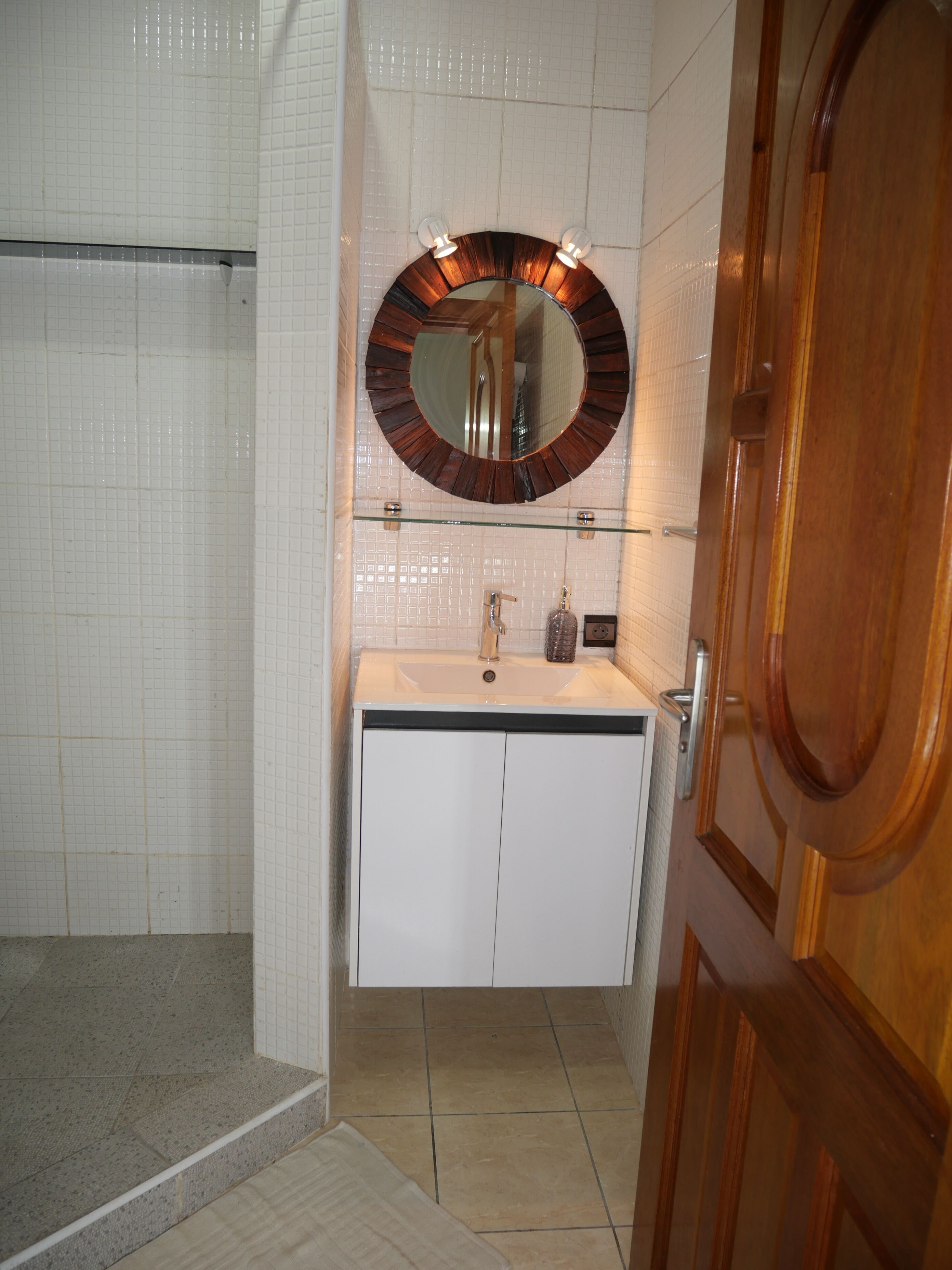 A bathroom with a shower, a sink with a mirror, and a wooden door.