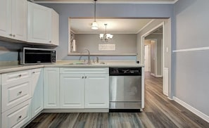 A kitchen with white cabinets, a microwave, a dishwasher, and a chandelier. - Welcoming 2-bedroom house in charming Enid. (Enid)
