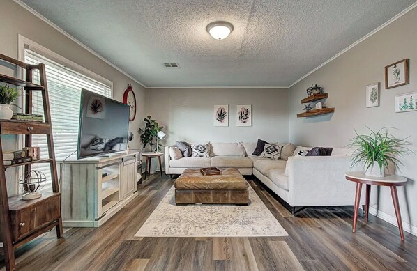 A living room with a sofa, ottoman, wooden floor, and a ceiling light. - Welcoming 2-bedroom house in charming Enid. (Enid)