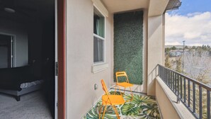 A balcony with a view of a residential area, a small table, two chairs, and a green wall.