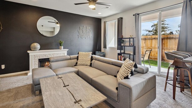 A modern living room with a sectional sofa, a fireplace, a ceiling fan, and a sliding glass door to a backyard.