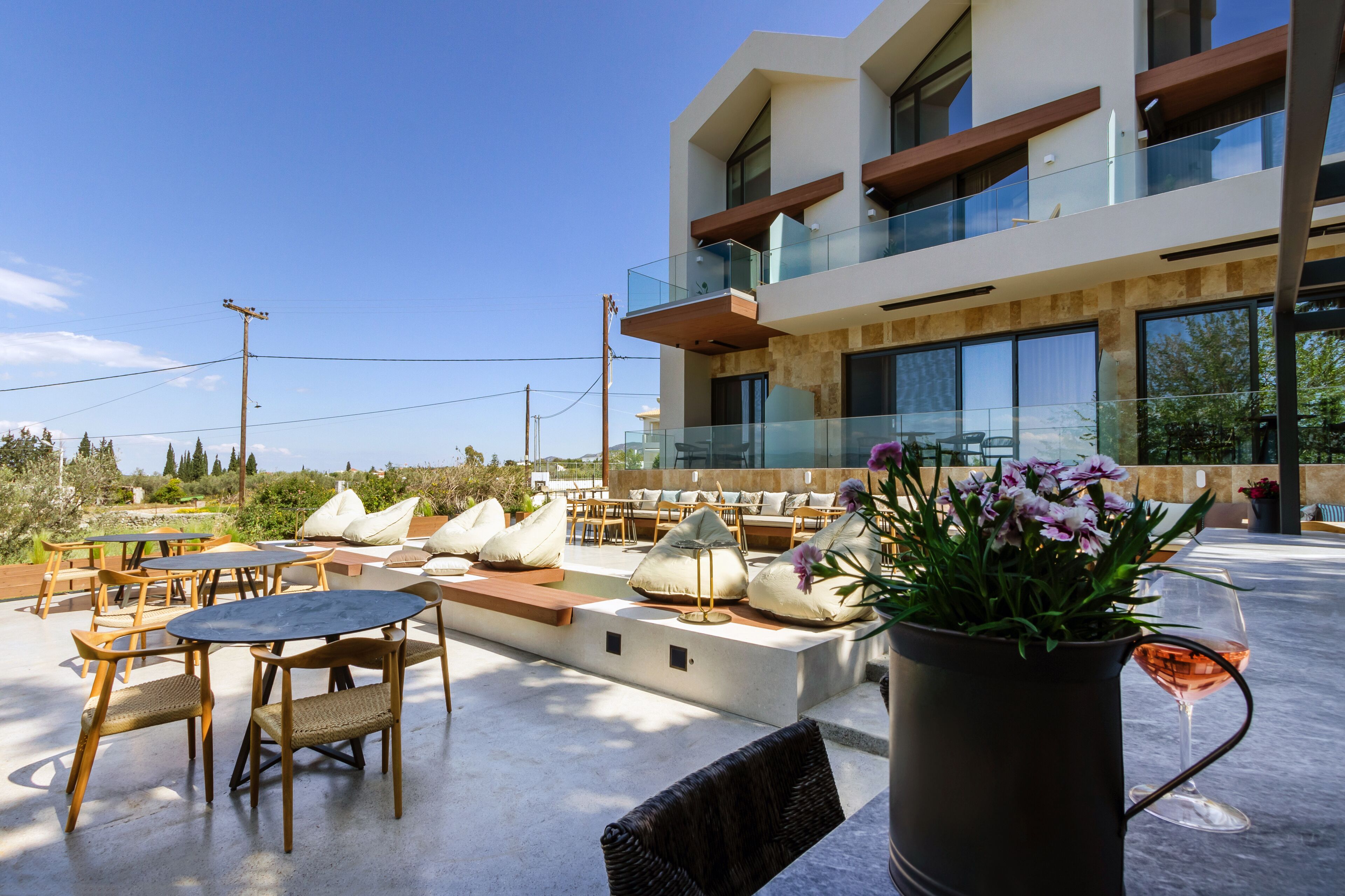 A modern outdoor seating area with tables and chairs, a large planter with flowers, and a building with large windows and balconies.