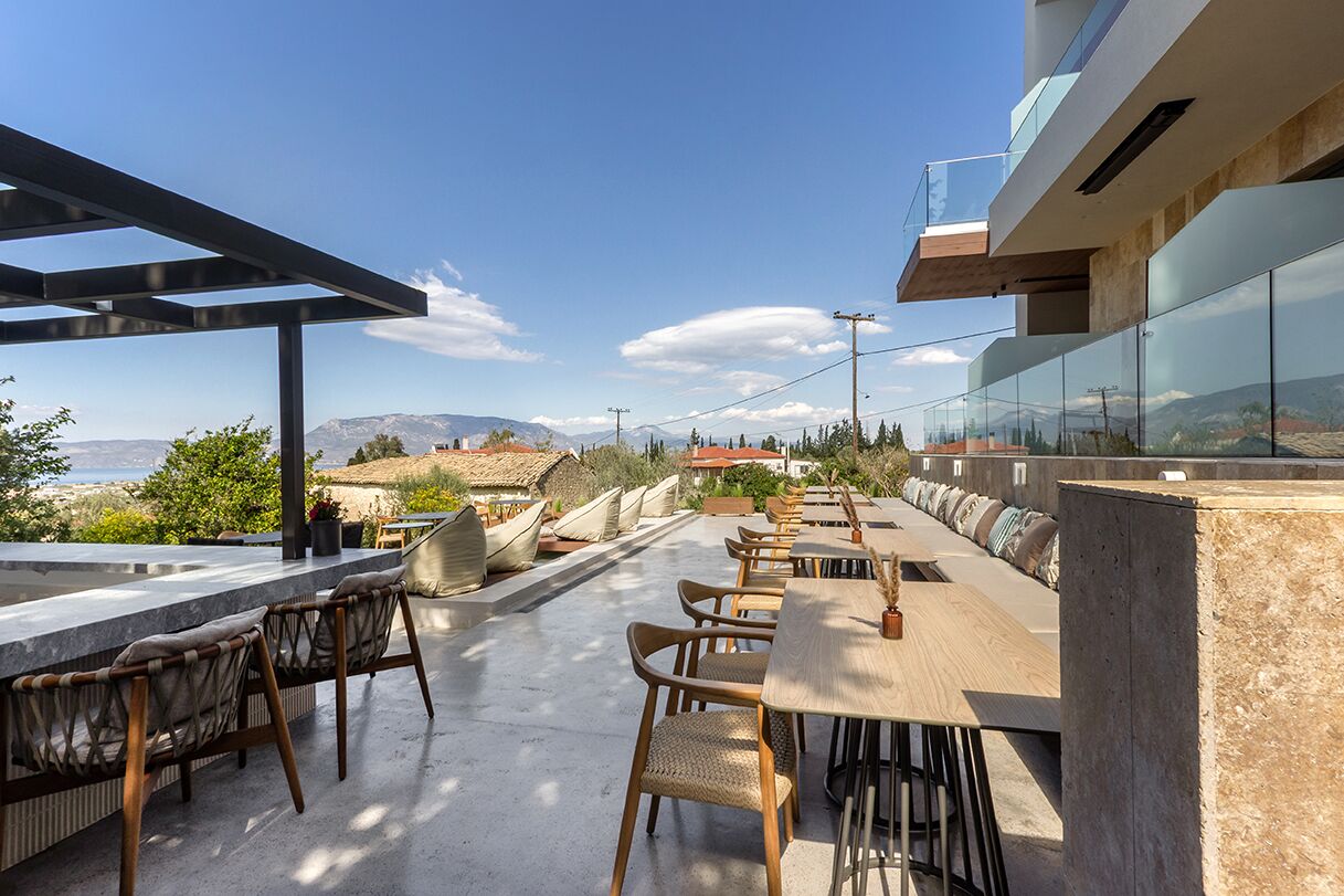 Un espacio de comedor al aire libre con vistas al mar y a las montañas, con mobiliario moderno y una pérgola.