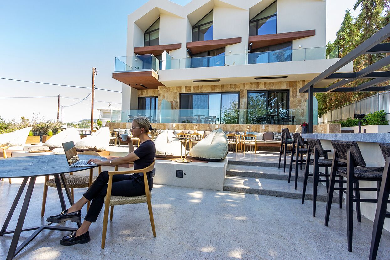 A modern outdoor seating area with a laptop on a table, surrounded by cushioned chairs and sofas.