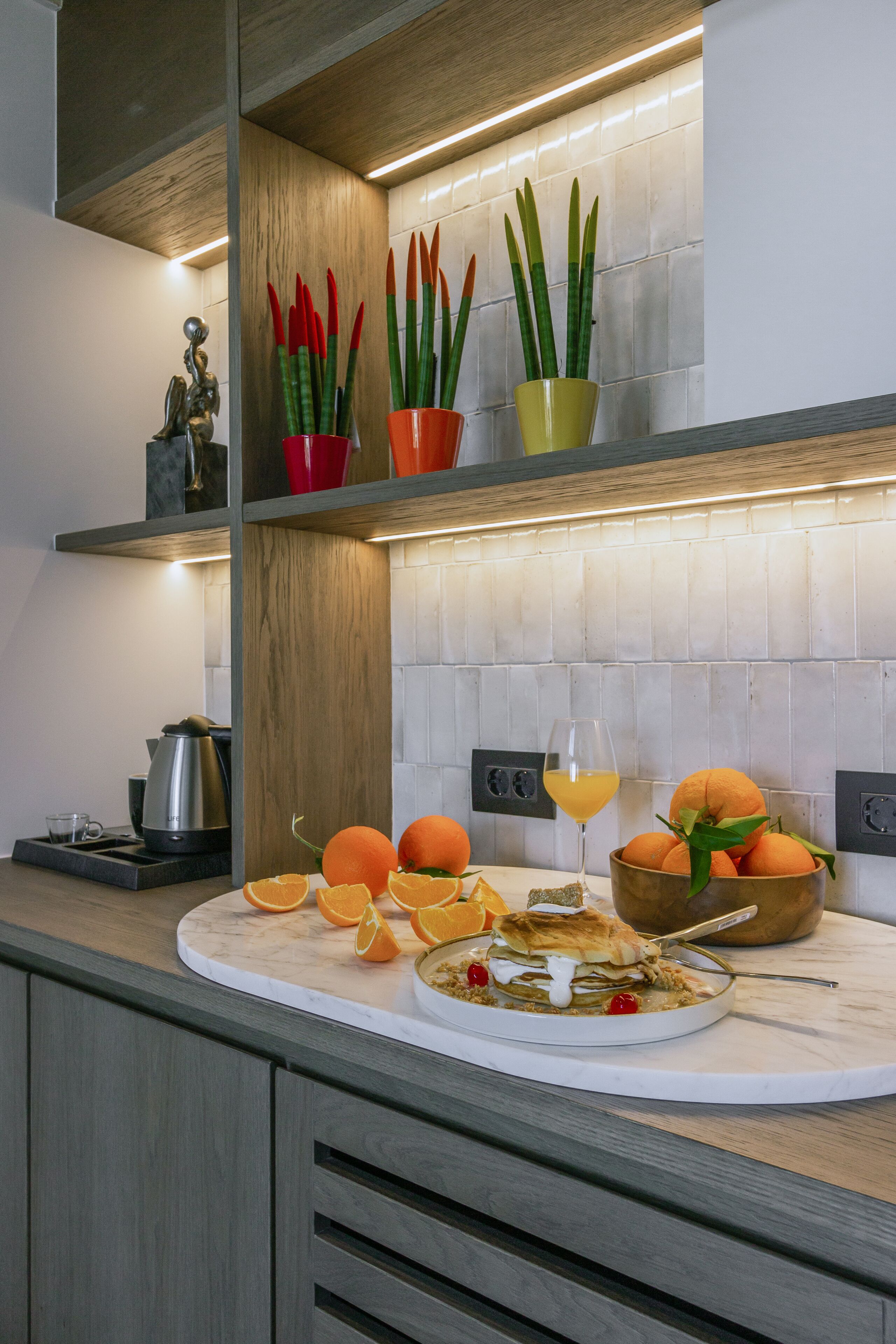 A kitchen counter with a marble top, a coffee maker, a fruit bowl with oranges, and a glass of orange juice.