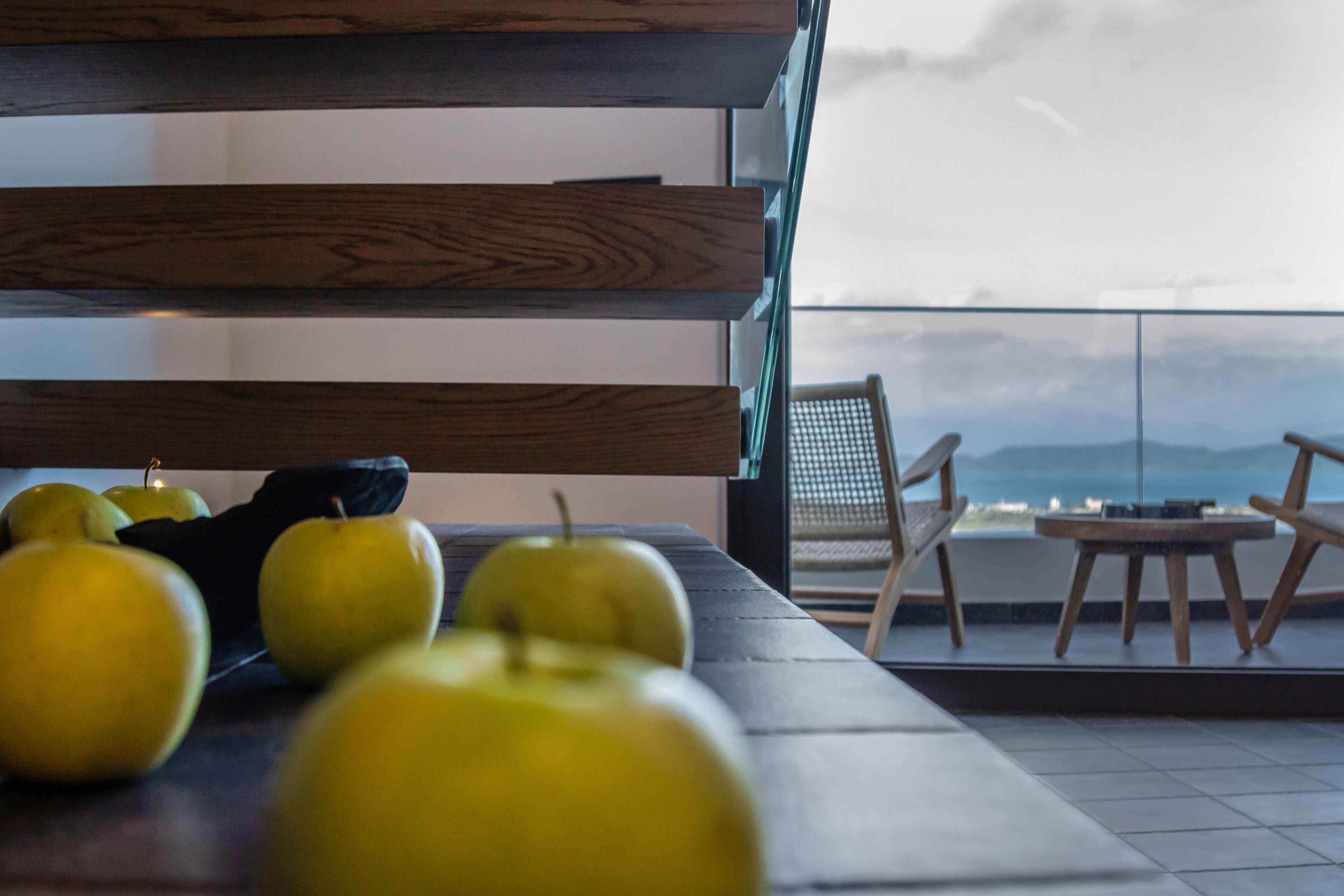 A table with apples and a chair on a balcony with a view of the sky and mountains.