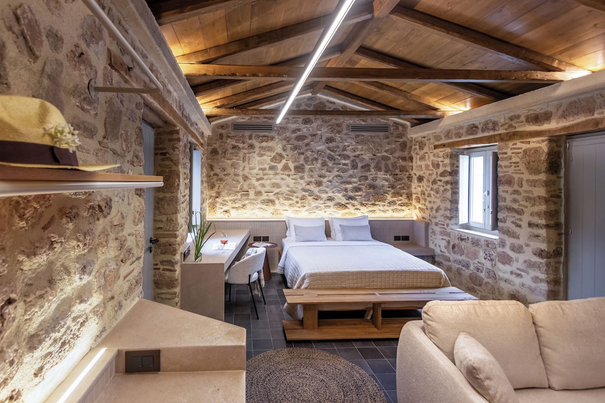 Un dormitorio rústico con paredes de piedra, techo de madera, una cama, un escritorio y un sofá.