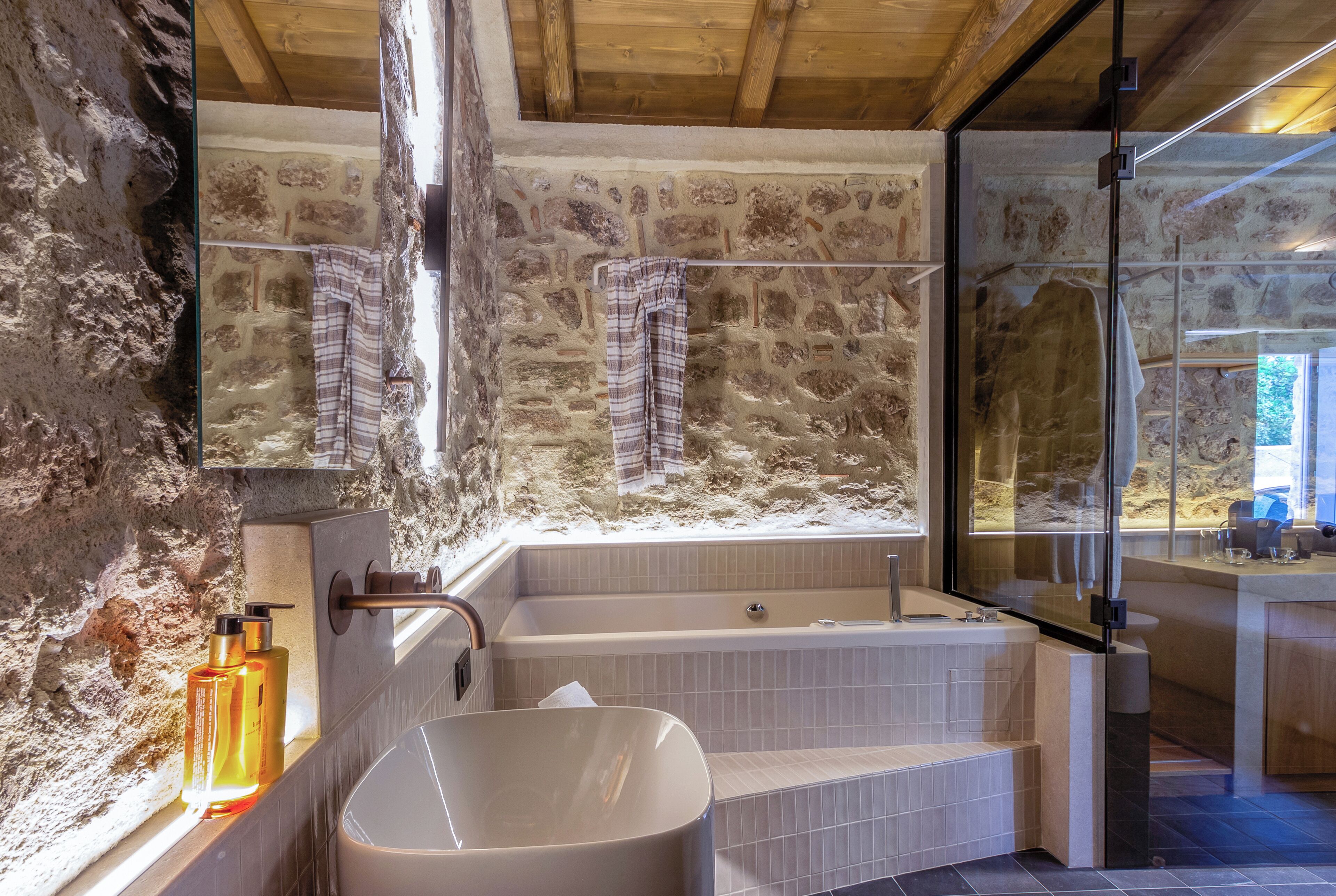 A bathroom with a stone wall, a bathtub, a sink, and a window.