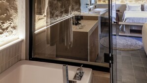 Un baño con bañera, ducha con mampara de vidrio y pared de piedra.