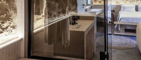 A bathroom with a bathtub, a glass-enclosed shower, and a stone wall.