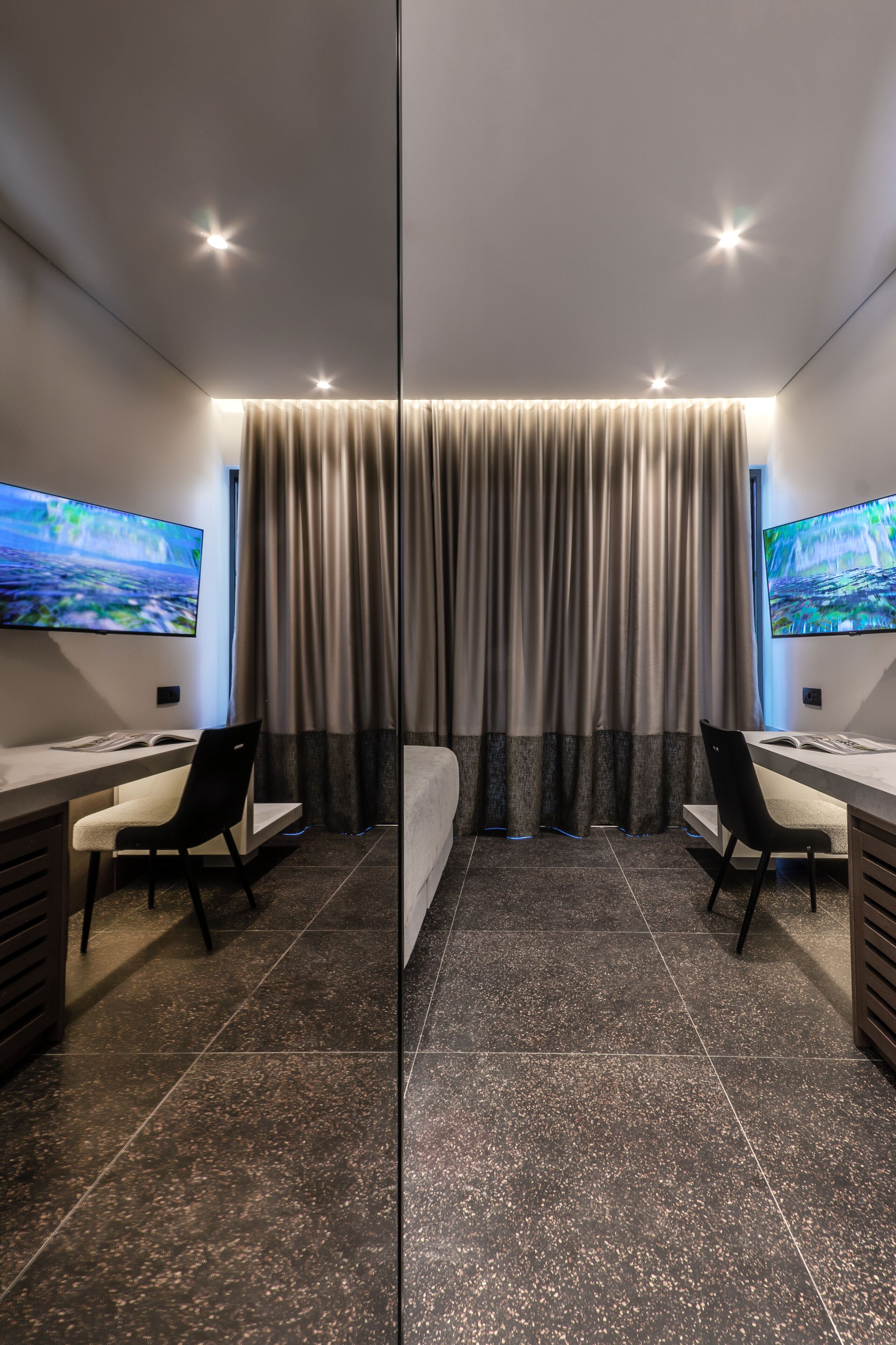 Een moderne hotelkamer met een groot bed, twee bureaus, twee stoelen en twee flatscreentelevisies.