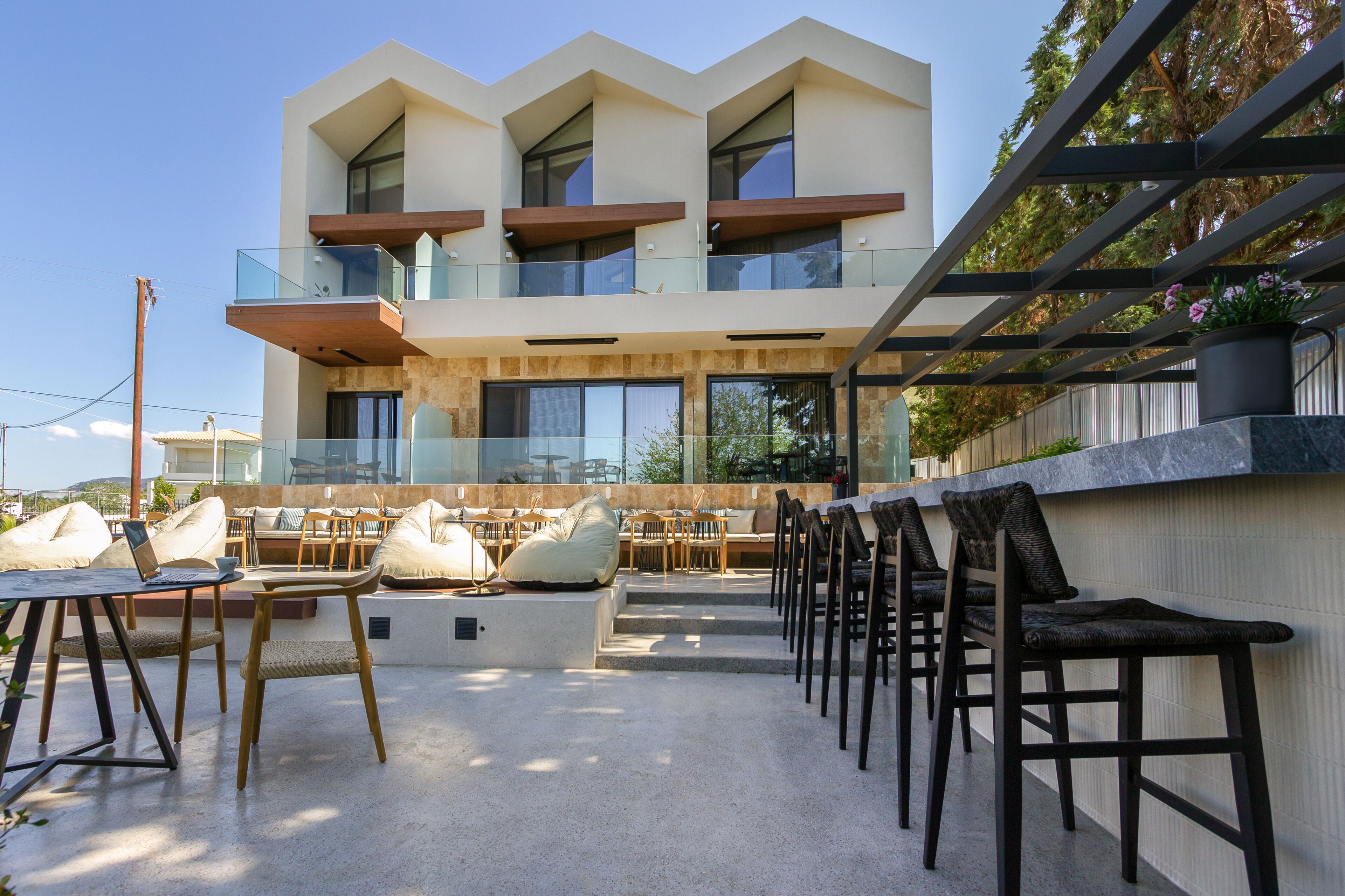 A modern outdoor seating area with multiple chairs and tables, a balcony with glass railings, and a building with large windows and a flat roof.