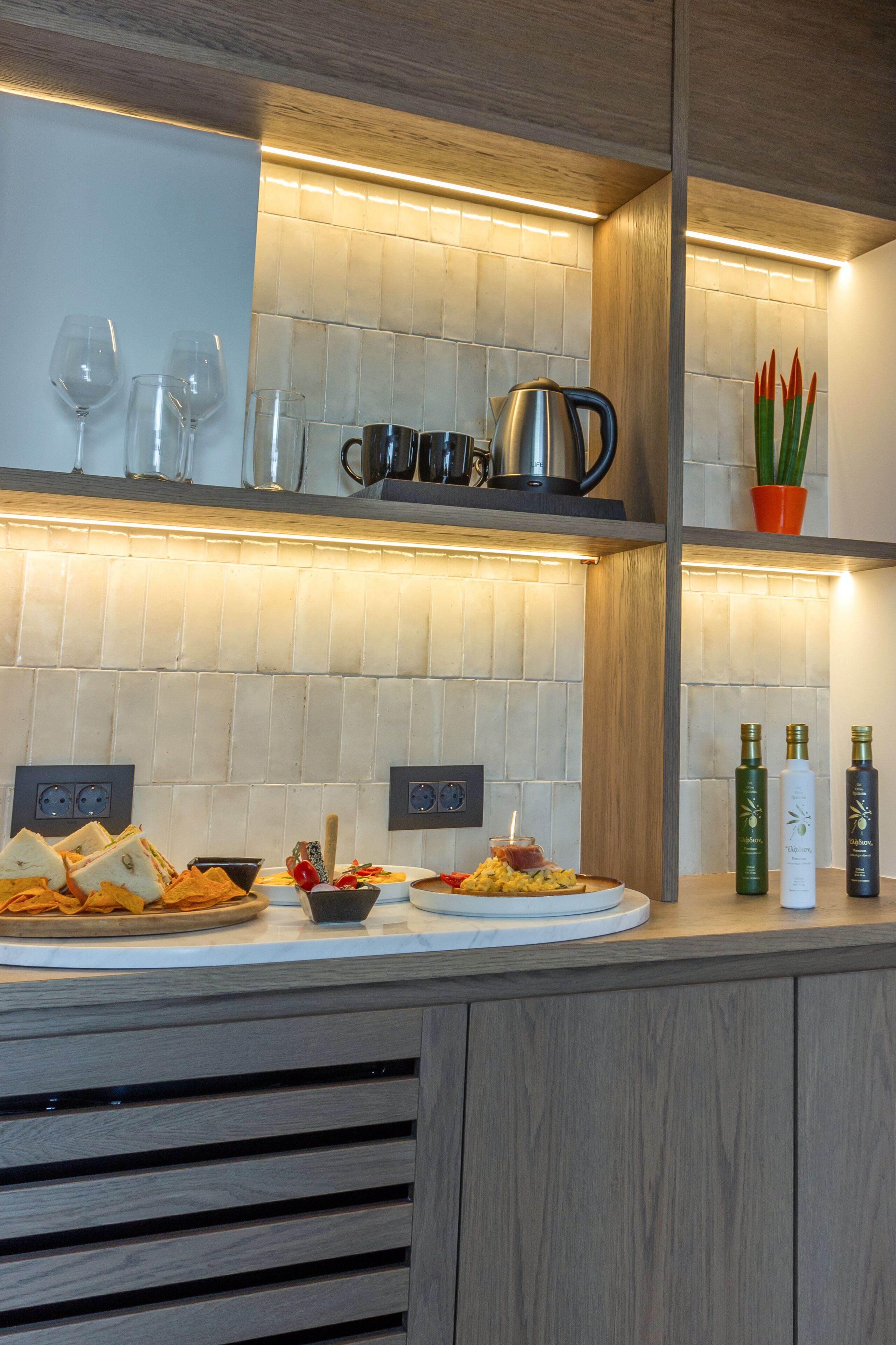 Una cocina moderna con salpicadero de azulejos blancos, armarios de madera y encimera con alimentos y utensilios de cocina.