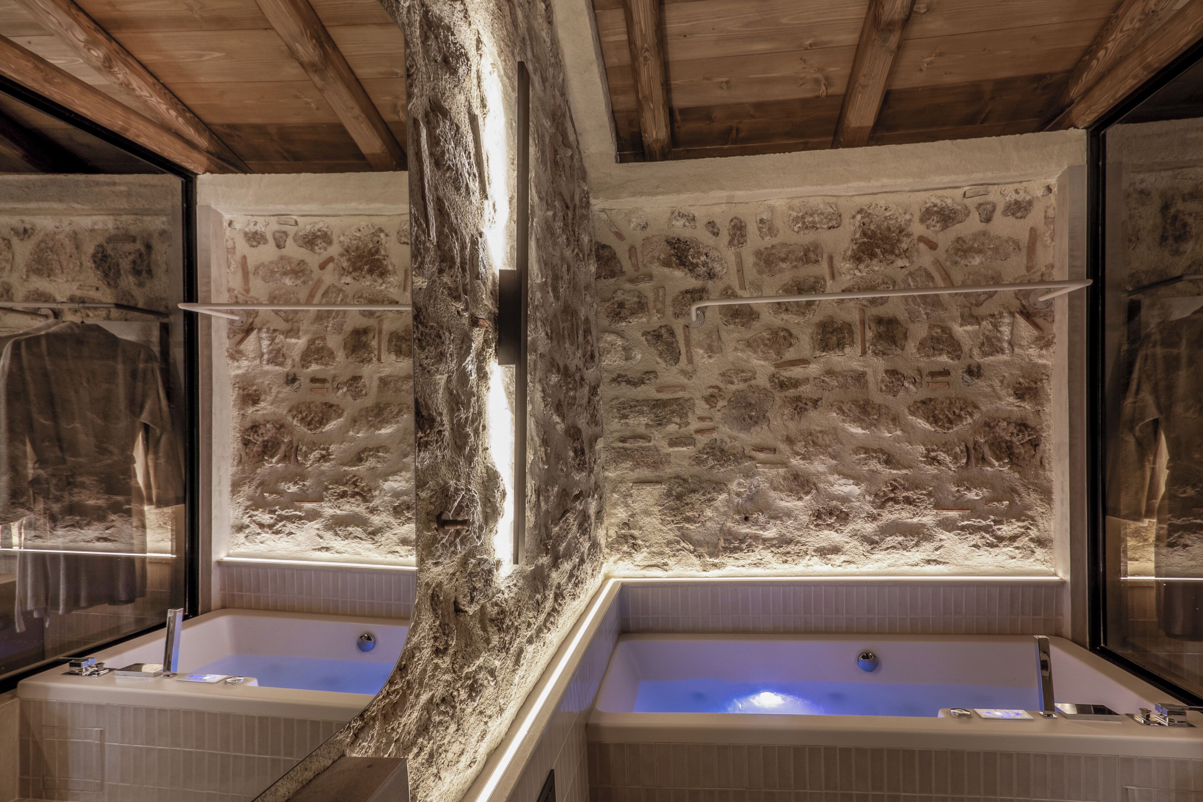 A bathroom with two large tubs, stone walls, and wooden beams.