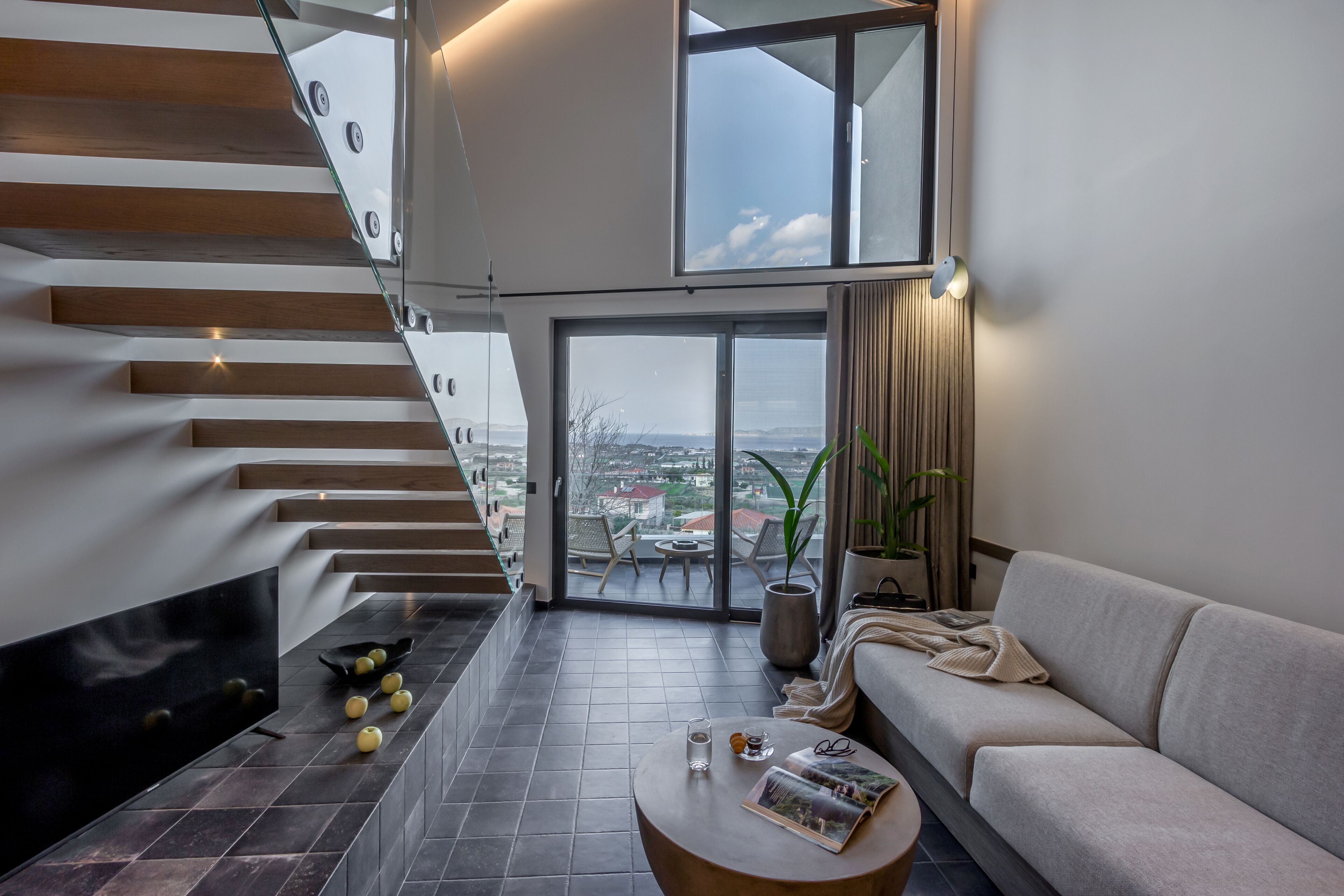 Ein modernes Wohnzimmer mit Treppe, Sofa, Couchtisch und Blick auf die Stadt.