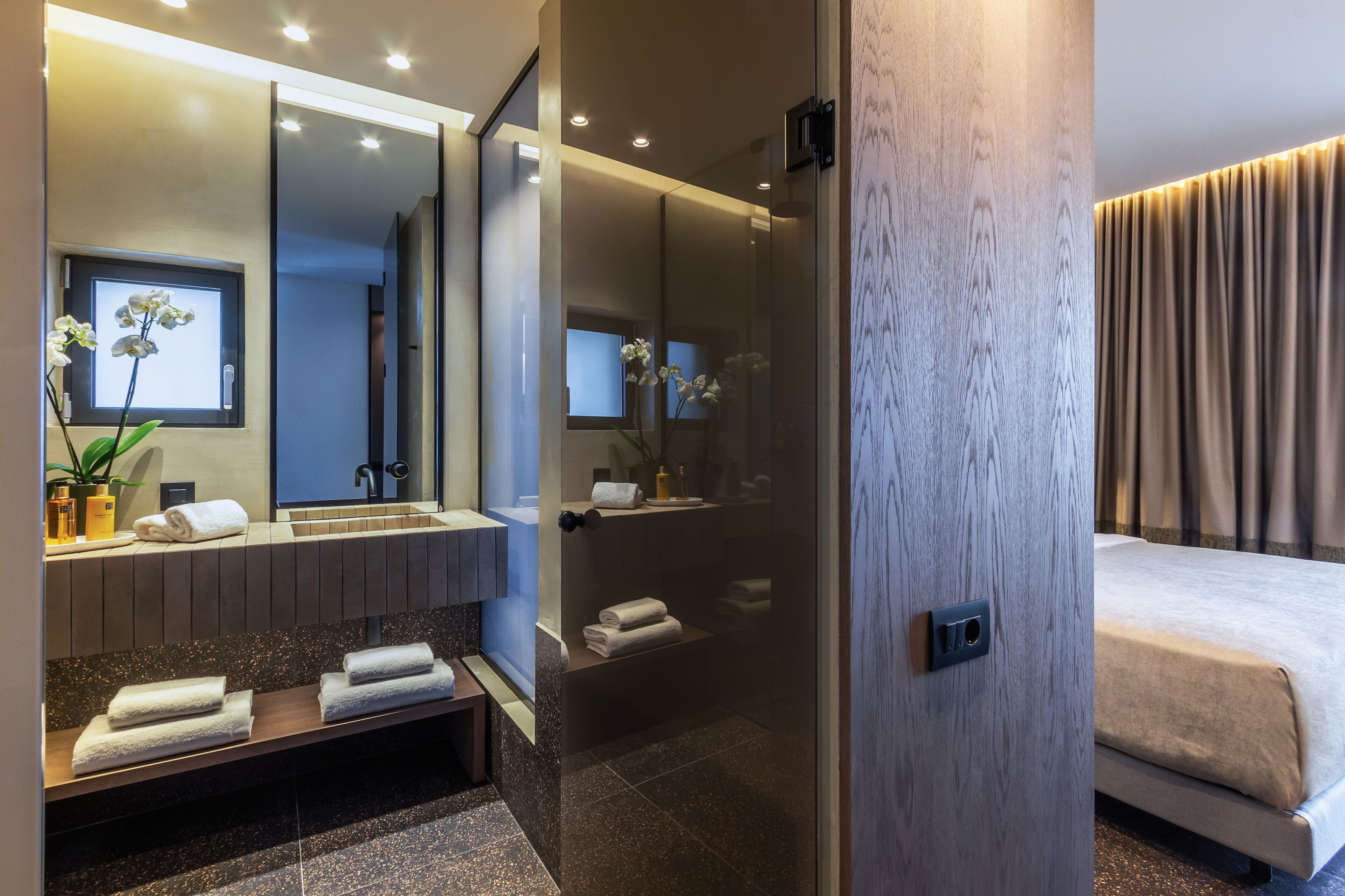 Un baño moderno con un espejo grande, zona de ducha y una cama con vistas a las cortinas.