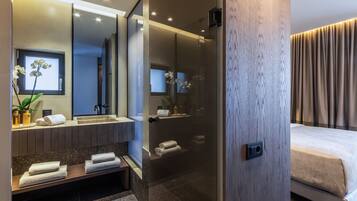 Un baño moderno con un espejo grande, zona de ducha y una cama con vistas a las cortinas.