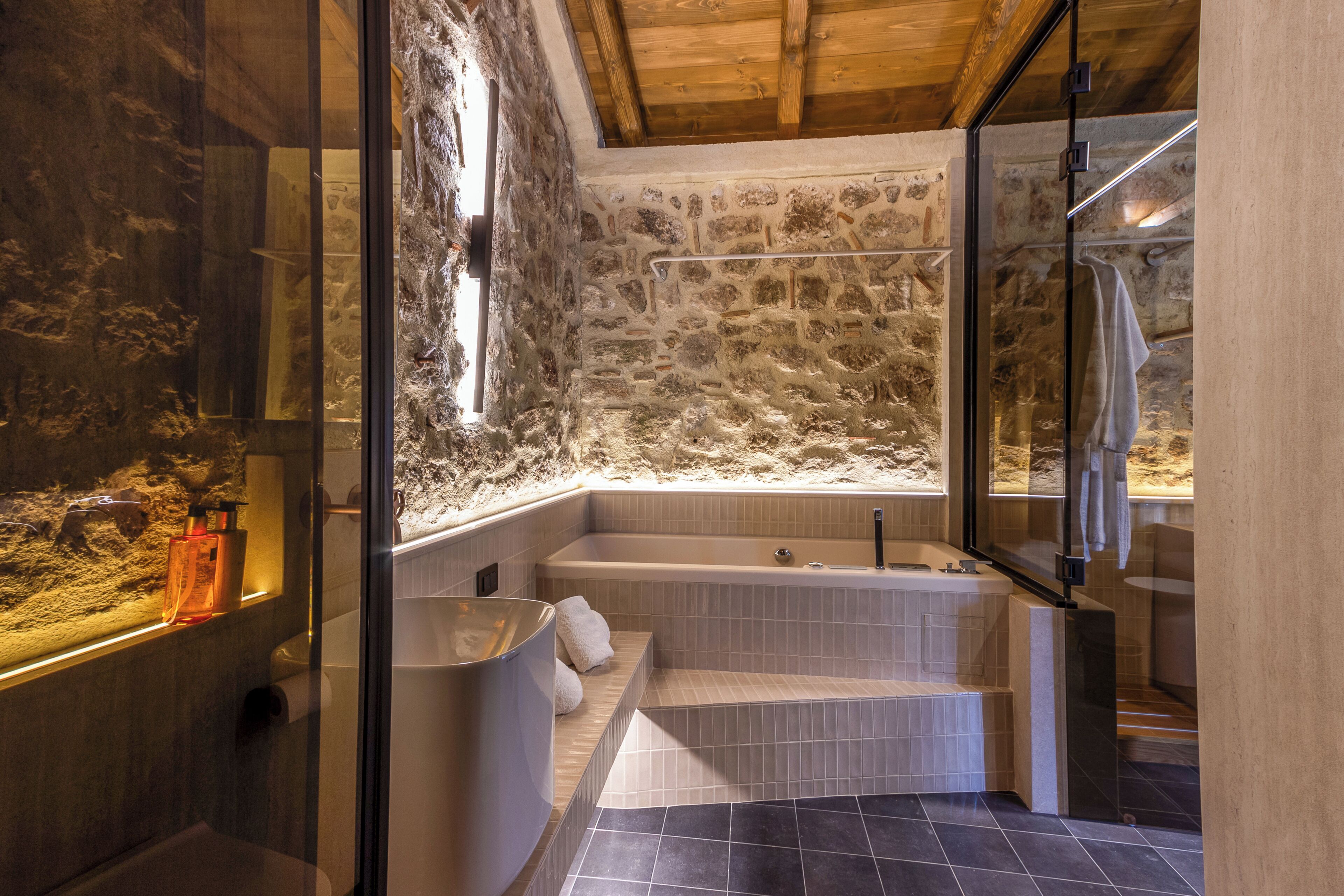 Ein modernes Badezimmer mit Steinwand, einer Duschkabine aus Glas und einer eingebauten Badewanne.