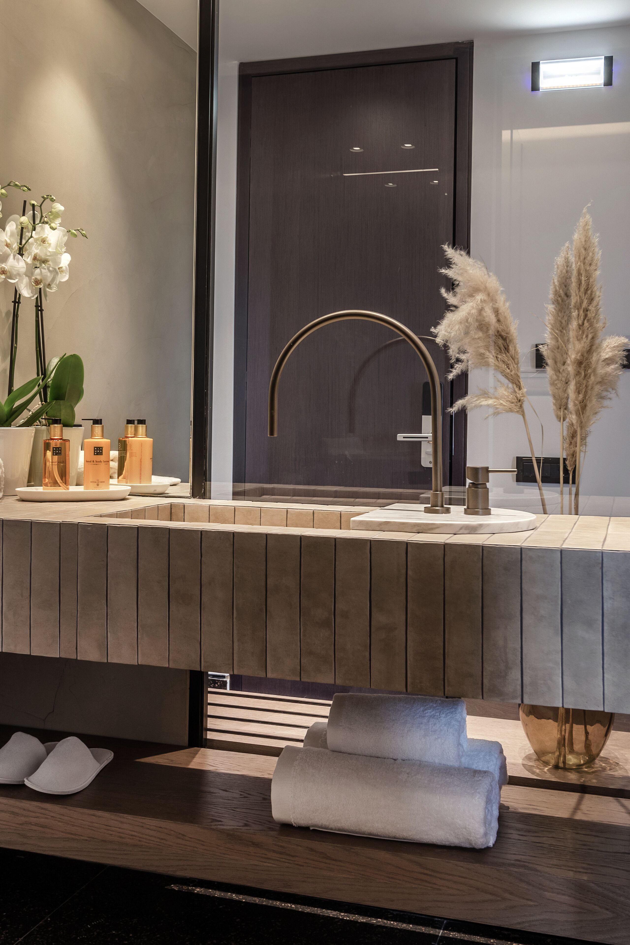 A modern bathroom with a large mirror, a gold faucet, and a wooden vanity.