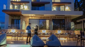 Un edificio moderno de dos pisos con un bar en la azotea que incluye asientos al aire libre y una piscina.