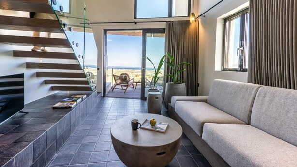 Una sala de estar moderna con un sofá, una mesa de centro y una escalera con barandas de vidrio.