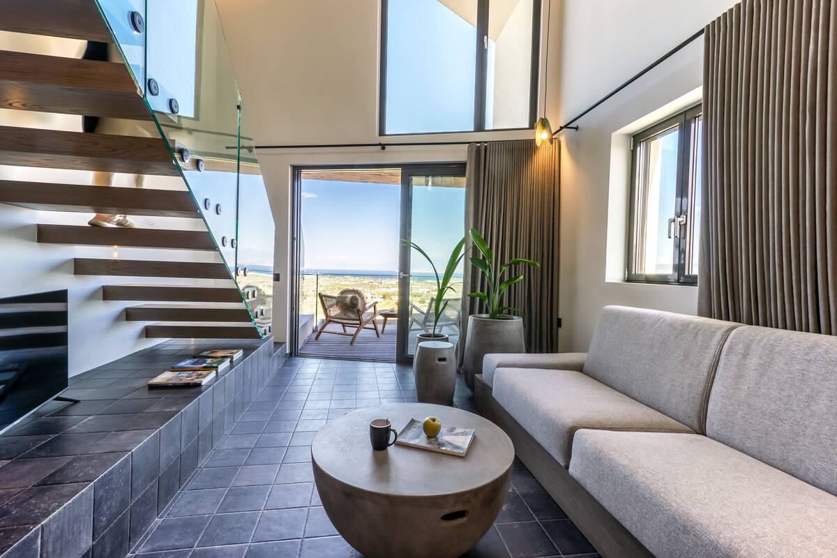 Una sala de estar moderna con un sofá, una mesa de centro y una escalera con barandas de vidrio.