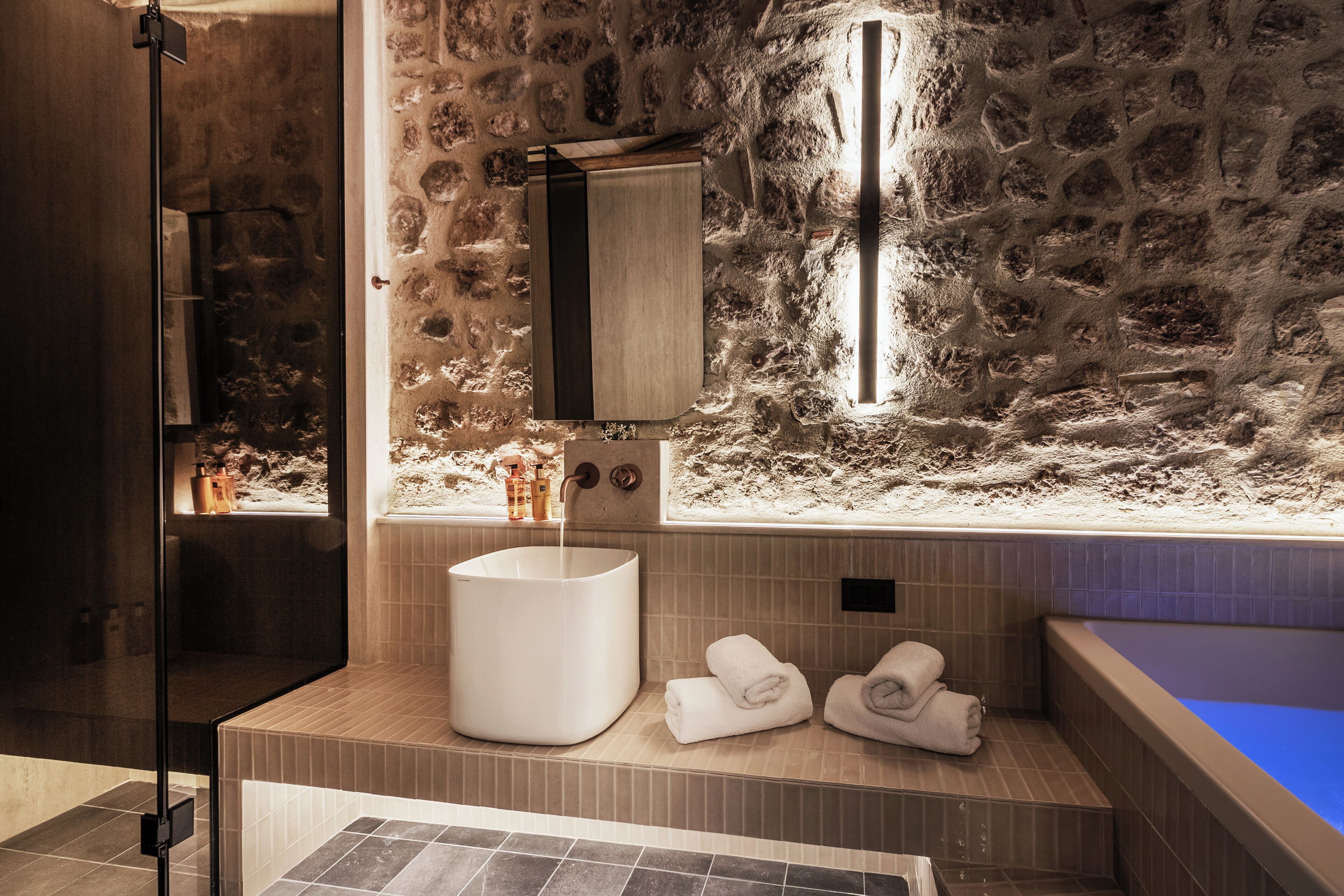 Une salle de bain moderne avec un mur en pierre, un grand lavabo et une baignoire.