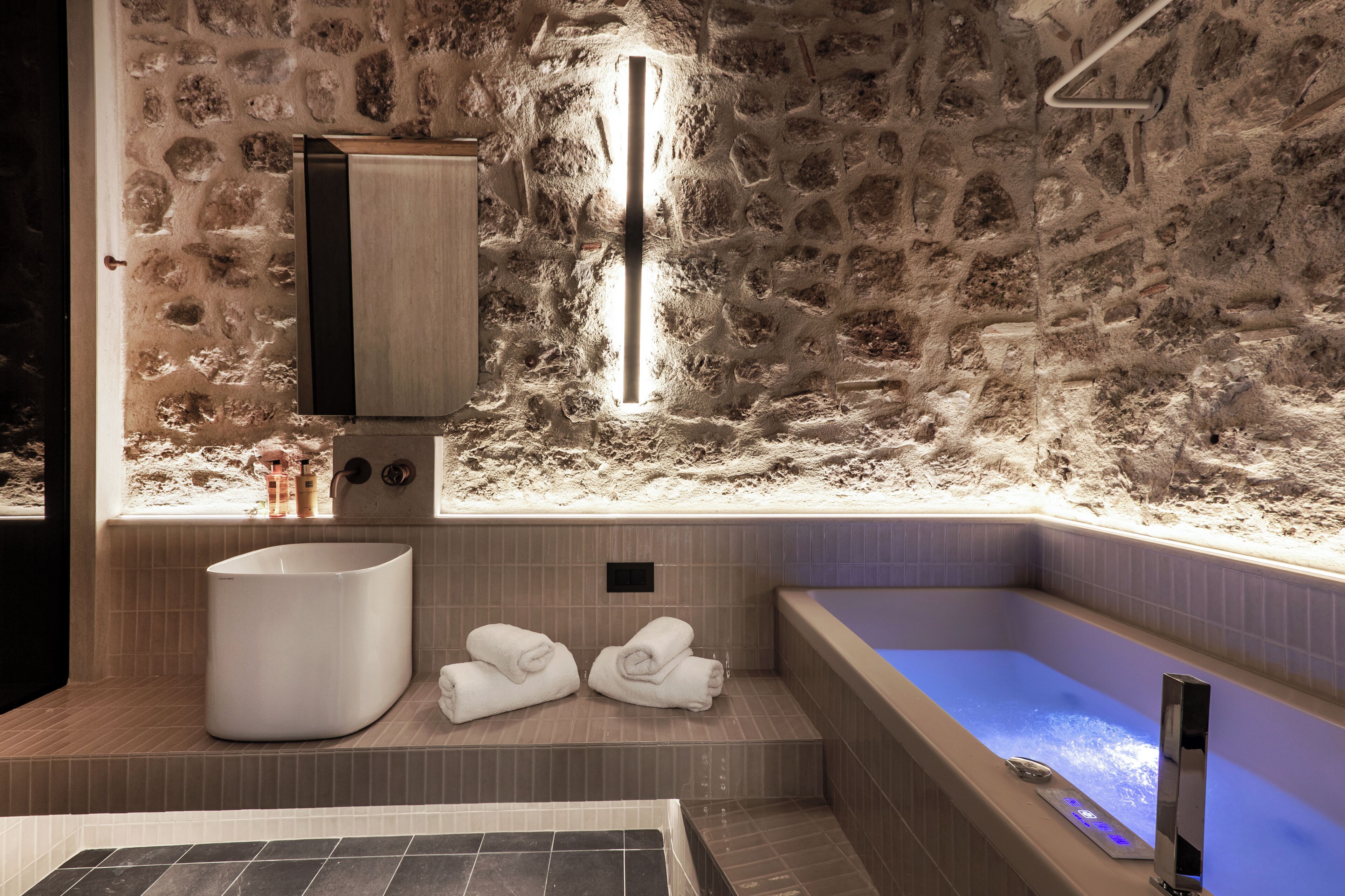 A modern bathroom with a stone wall, a large bathtub, and a separate shower area.