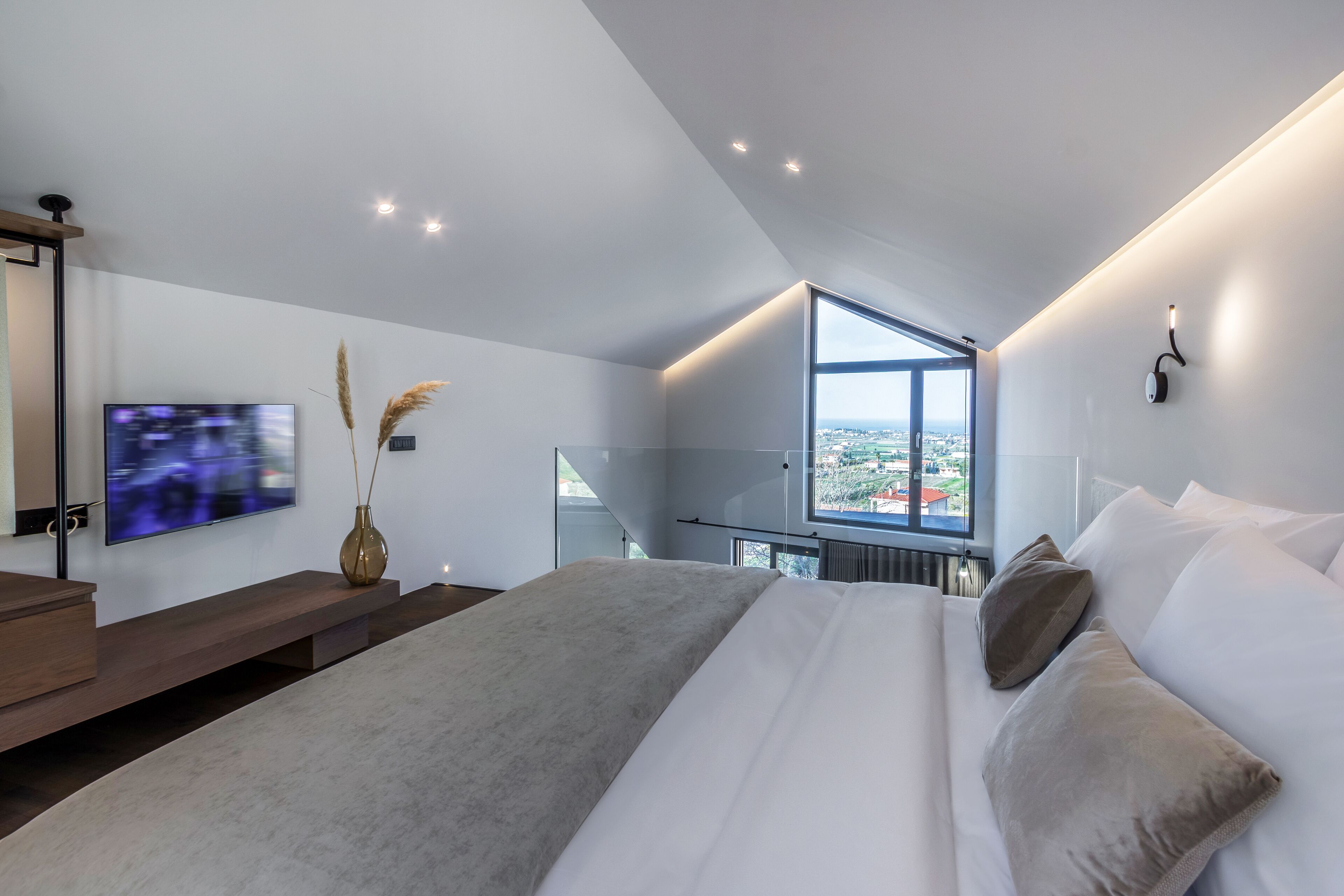 Une chambre moderne dotée d’un grand lit, d’une télévision, d’une fenêtre donnant sur la ville et d’un design minimaliste.