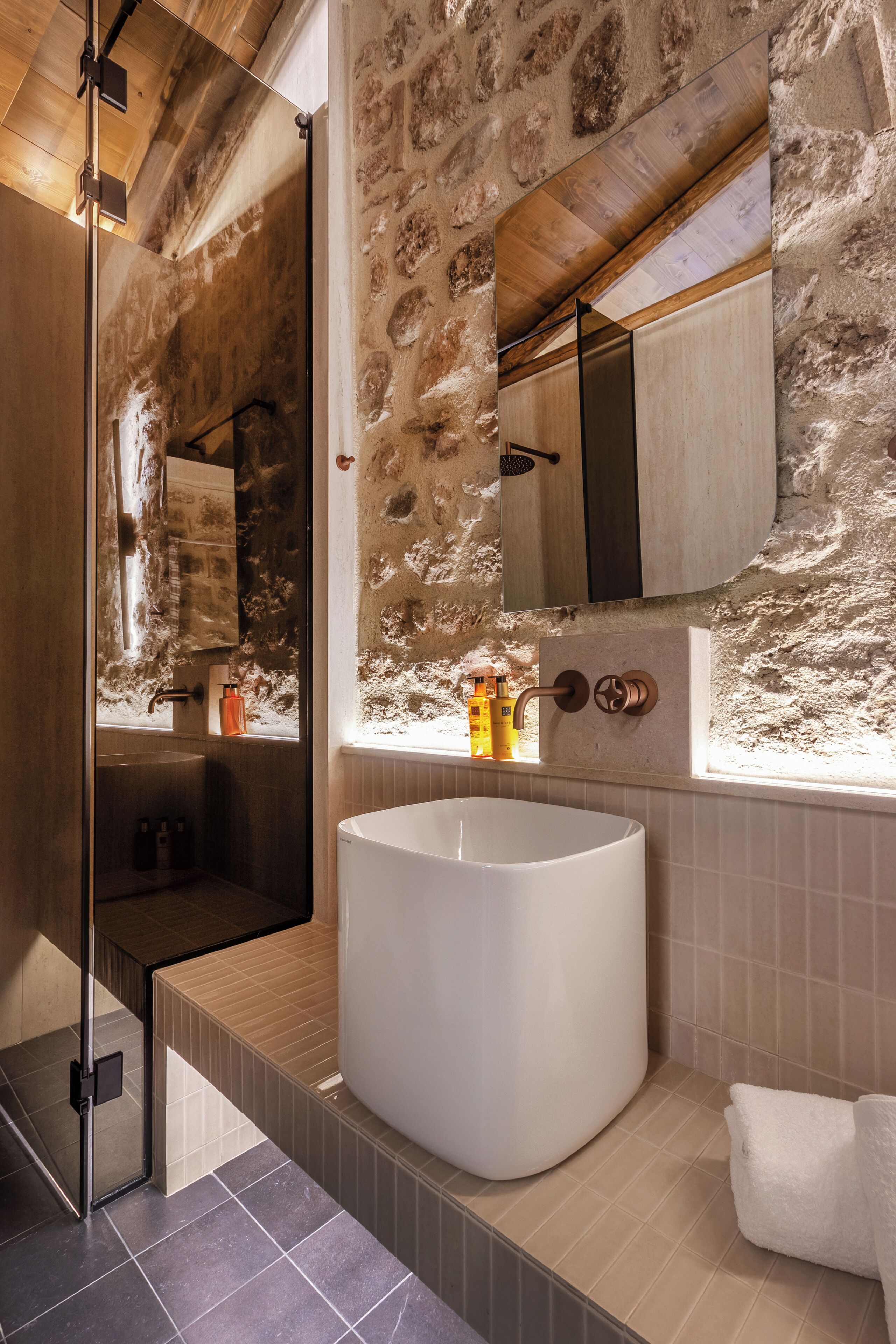 Ein Badezimmer mit Steinwand, einer großen weißen Badewanne und einem Spiegel über dem Waschbecken.