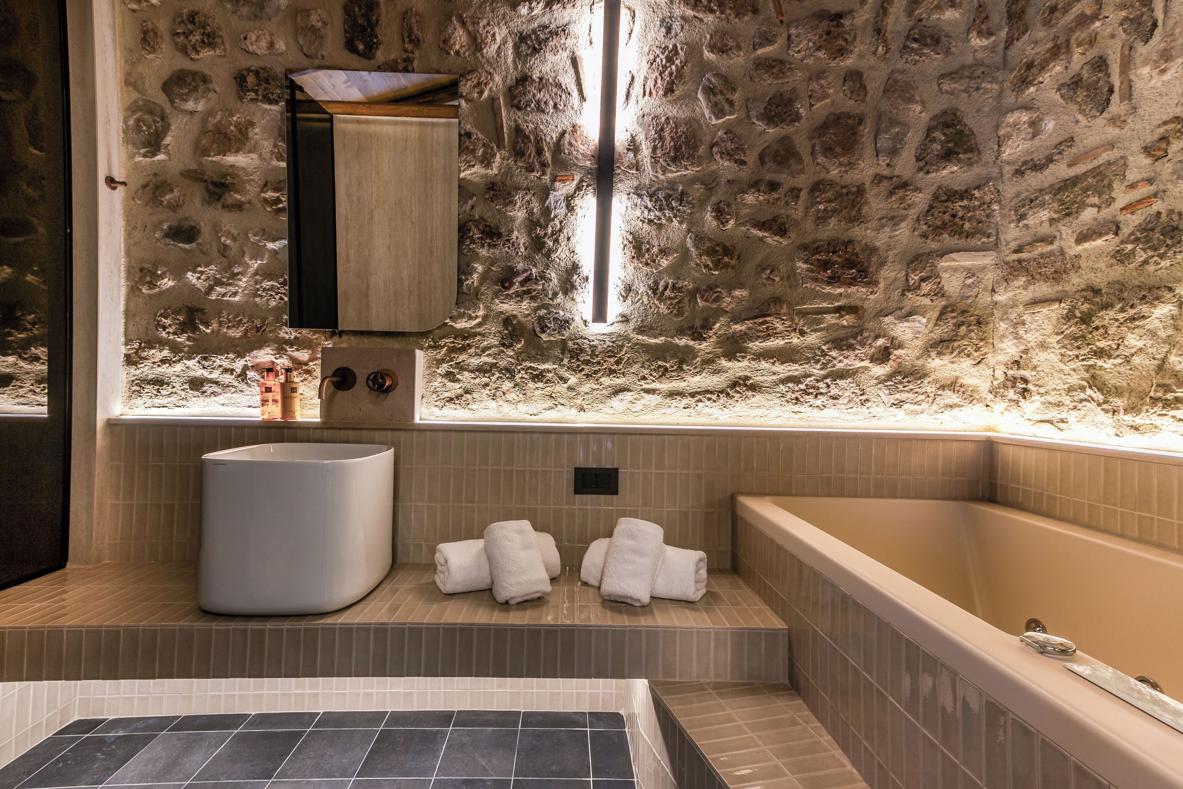 Une salle de bain avec un mur en pierre, une baignoire, un lavabo et des serviettes.
