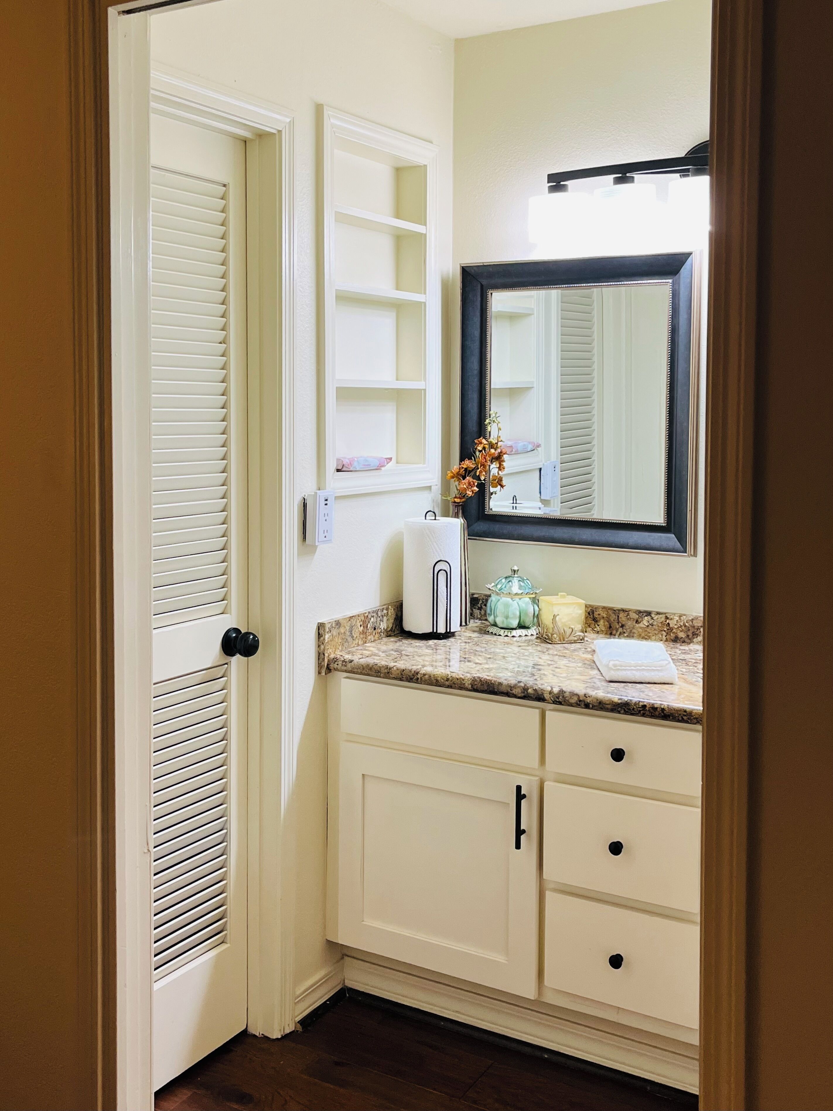 A bathroom with a white vanity, a mirror, and a door with louvered glass.