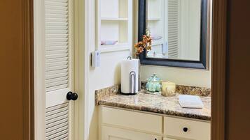 A bathroom with a white vanity, a mirror, and a door with louvered glass.