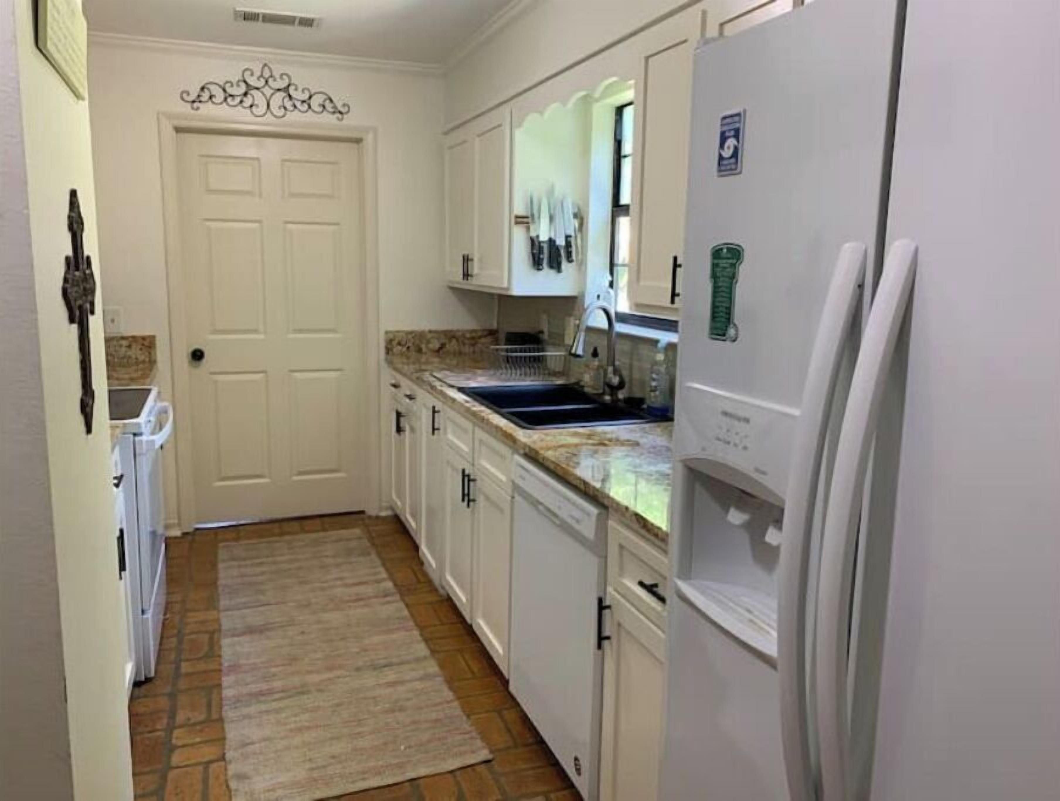 A kitchen with white cabinets, a granite countertop, a built-in oven, and a refrigerator.