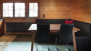 Un interior de madera con una mesa, sillas, un ventanal con persianas y un radiador.