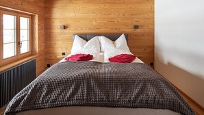 Un dormitorio con pared de madera, una ventana, una cama con manta gris y roja, y cabecero gris.