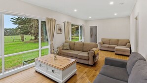 Un salón amplio con ventanas grandes, un sofá color beige, un sofá gris y un armario blanco.