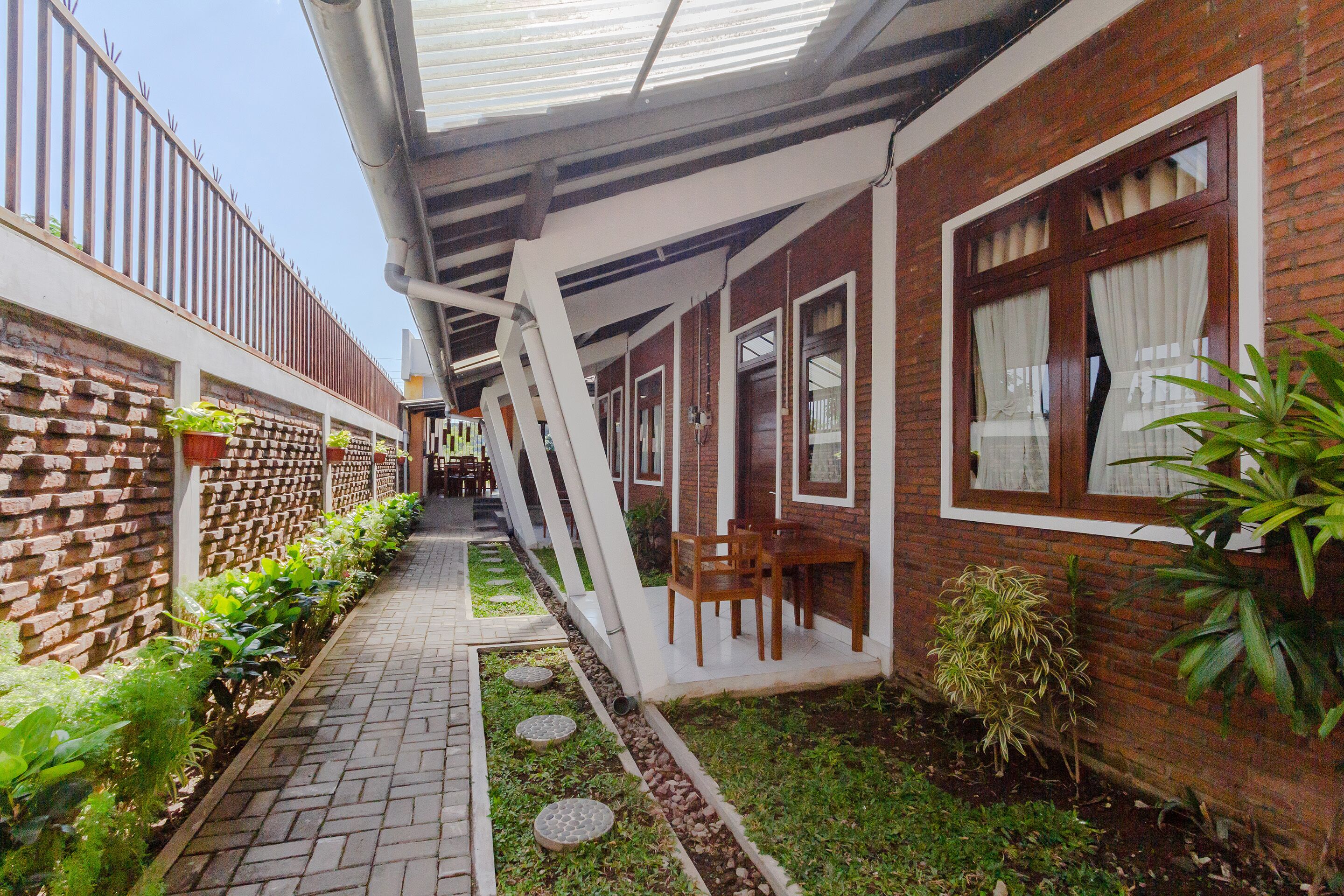 A covered outdoor corridor with brick walls, potted plants, and a pathway leading to a seating area.