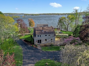A two-story house with a front yard, a driveway, and a view of a lake.